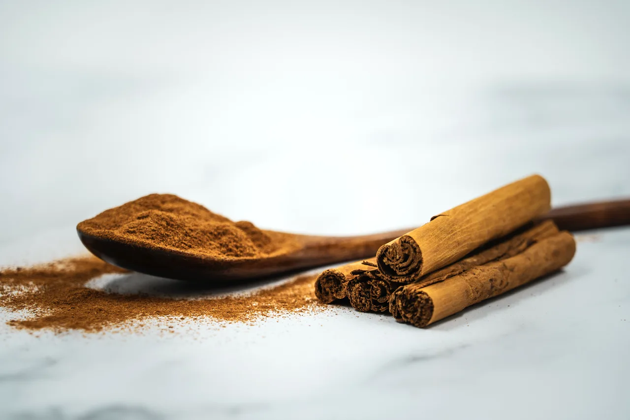 Ground cinnamon on a wooden spoon with cinnamon sticks on marble