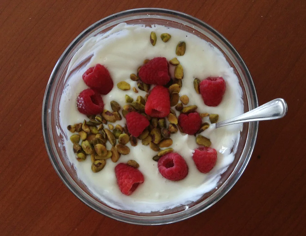 Plain Greek yogurt in a glass bowl with raspberries and pistachios