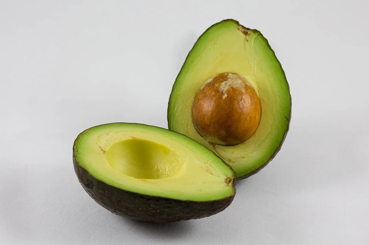 A halved avocado, one side hollow and the other holding the round pit
