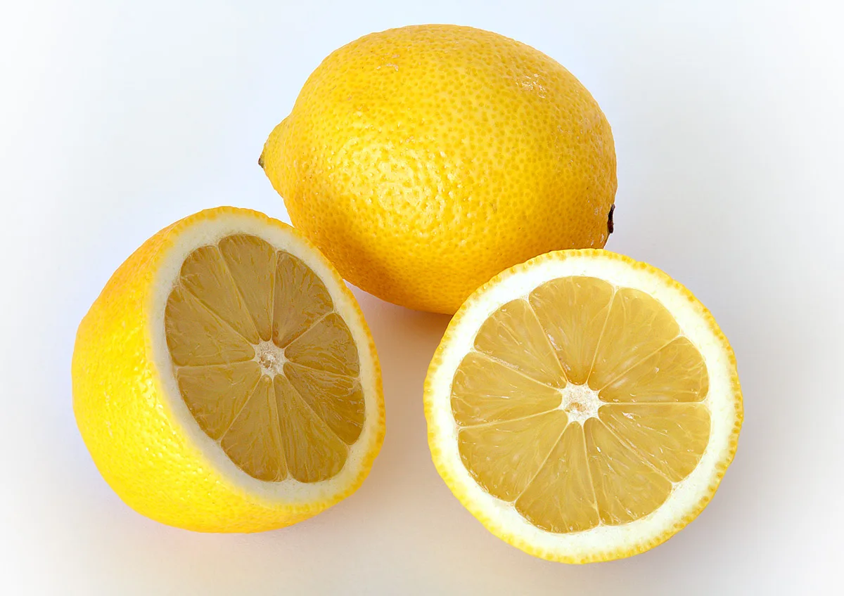 Whole lemon and halved lemon showing bright yellow flesh on white background
