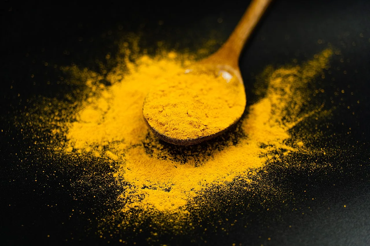 A spoonful of bright yellow ground turmeric against a black background